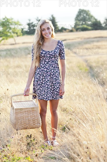 Happy teenage girl (16-17) standing in meadow, holding picnic basket. Photo : Take A Pix Media