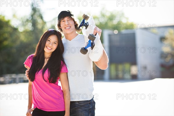 Young multi-racial couple posing with skateboard. Photo : Take A Pix Media