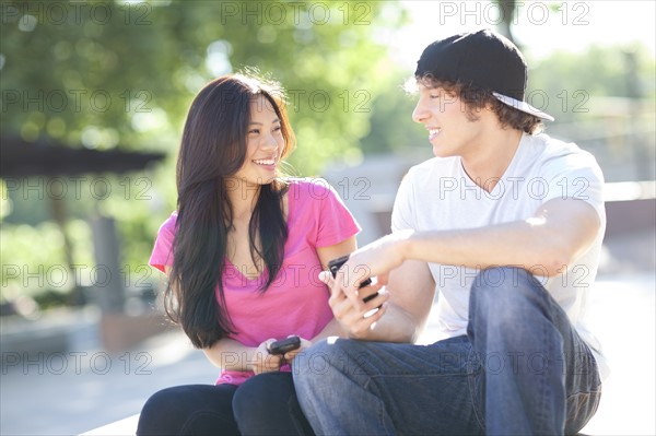 Young multi-racial couple sitting together playing with their mobile phones. Photo : Take A Pix Media