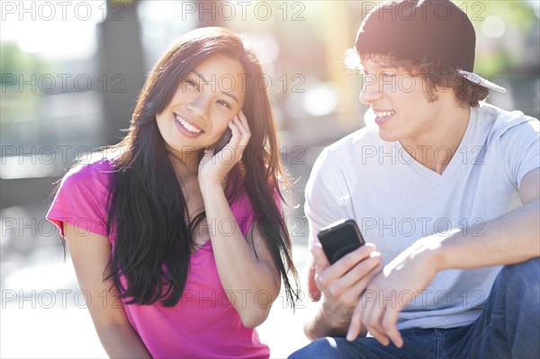 Young multi-racial couple sitting together playing with their mobile phones. Photo : Take A Pix Media