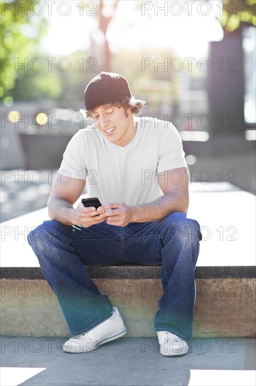 Young man sitting outdoors, text messaging. Photo: Take A Pix Media