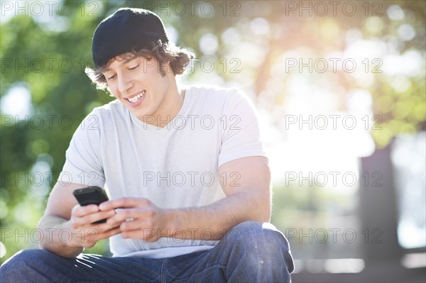 Young man sitting outdoors, text messaging. Photo : Take A Pix Media