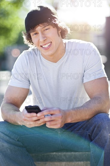 Young man sitting outdoors, text messaging. Photo : Take A Pix Media