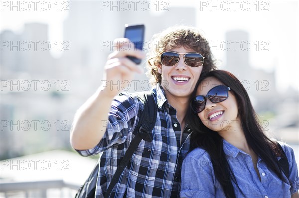 USA, Washington, Seattle, Couple wearing sunglasses photographing themselves with smart phone. Photo: Take A Pix Media