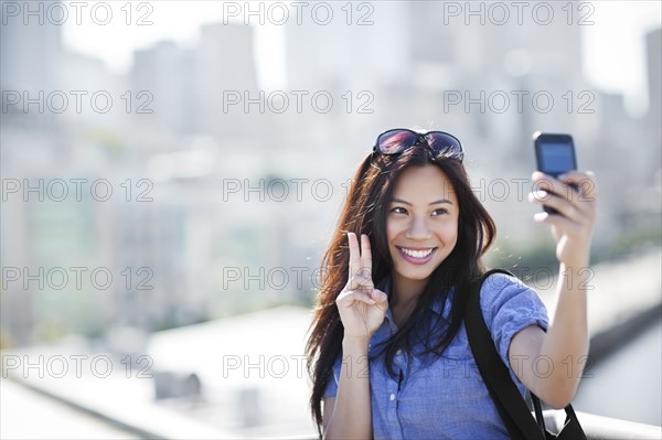 USA, Washington, Seattle, Woman photographing herself with smart phone outdoors. Photo: Take A Pix Media