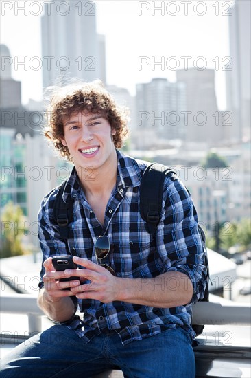 USA, Washington, Seattle, Man text messaging outdoors, skyline in background. Photo : Take A Pix Media