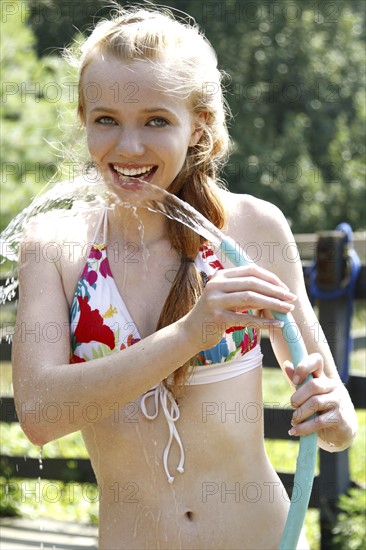 Teenage girl (14-15) wearing bikini drinking water from garden hose. Photo : Pauline St.Denis