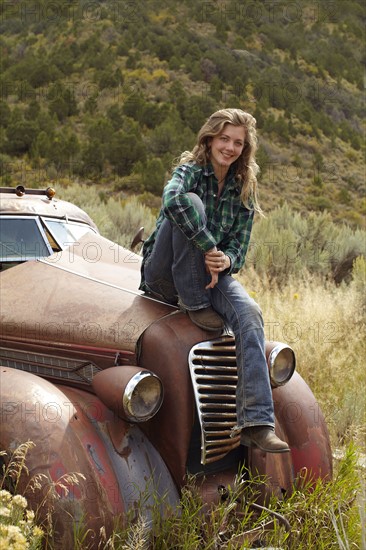 USA, Colorado, Portrait of woman resting on abandoned truck in desert. Photo : John Kelly