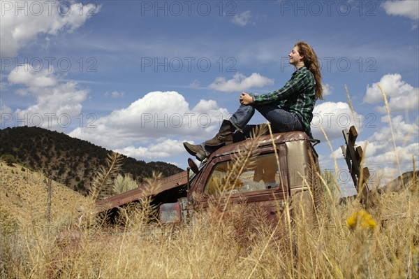 USA, Colorado, Woman resting on roof of abandoned truck in desert. Photo: John Kelly
