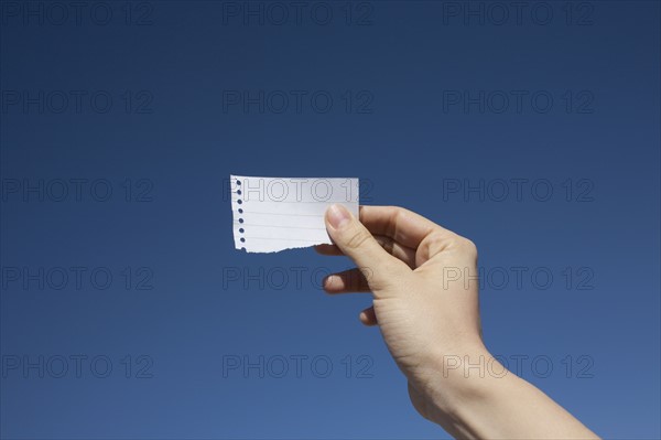 Hand of woman holding paper note against blue sky. Photo : Winslow Productions