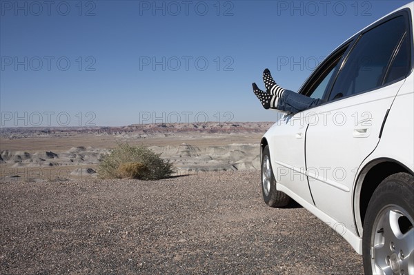 USA, Arizona, Winslow, Woman sticking feet out of car window parked in desert. Photo : Winslow Productions