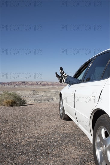 USA, Arizona, Winslow, Woman sticking feet out of car window parked in desert. Photo : Winslow Productions