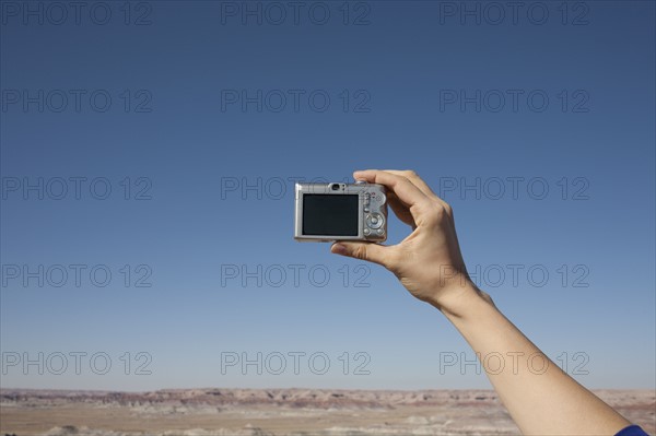 Hand of woman holding camera up against blue sky. Photo: Winslow Productions