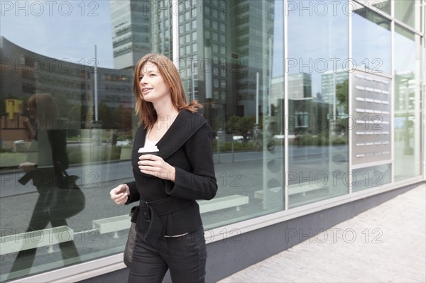 The Netherlands, Amsterdam, Businesswoman walking with coffee. Photo: Jan Scherders