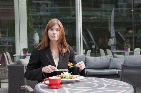 The Netherlands, Amsterdam, Businesswoman eating salad in sidewalk cafe. Photo : Jan Scherders