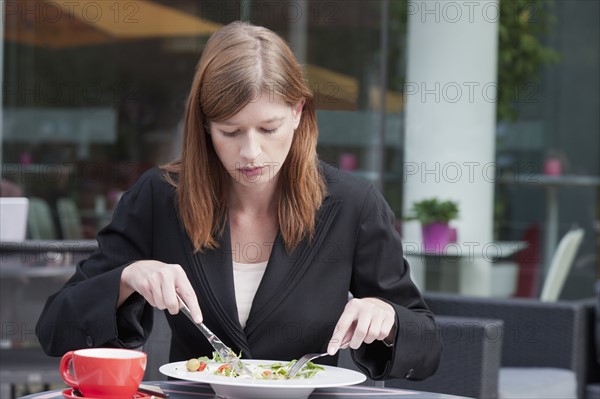 The Netherlands, Amsterdam, Businesswoman eating salad in sidewalk cafe. Photo : Jan Scherders