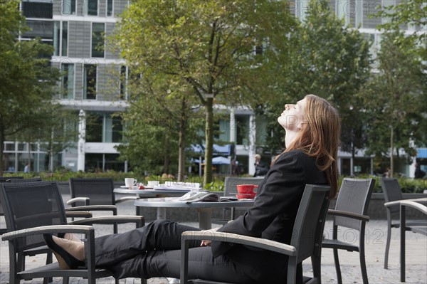 The Netherlands, Amsterdam, Businesswoman relaxing on chairs on sidewalk. Photo : Jan Scherders