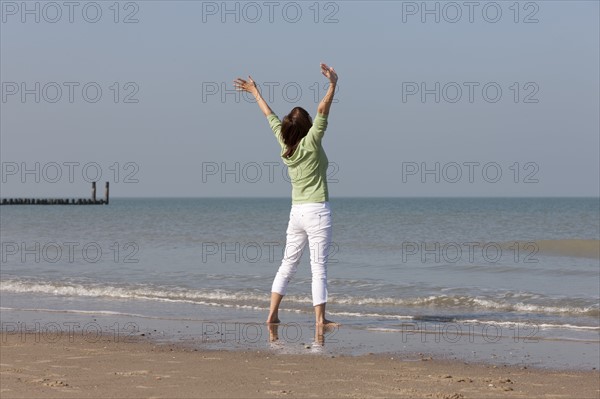 Woman on beach with arms raised. Photo : Jan Scherders