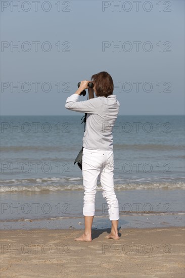 Woman on beach looking through binoculars. Photo : Jan Scherders