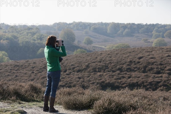 The Netherlands, Veluwezoom, Posbank, Woman in countryside looking through binoculars. Photo : Jan Scherders