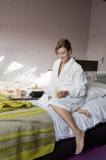Woman in bathrobe sitting in bedroom. Photo: Jan Scherders