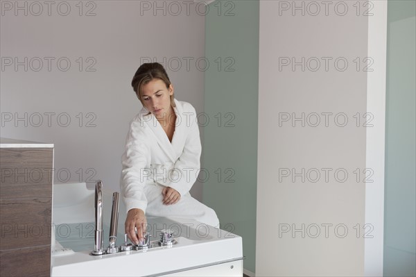 Woman in bathrobe pouring water into tub. Photo : Jan Scherders