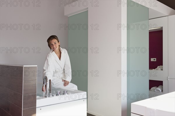Woman in bathrobe pouring water into tub. Photo : Jan Scherders