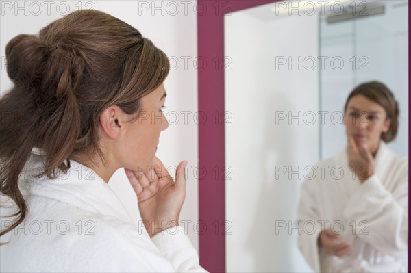 Woman looking in bathroom mirror. Photo : Jan Scherders