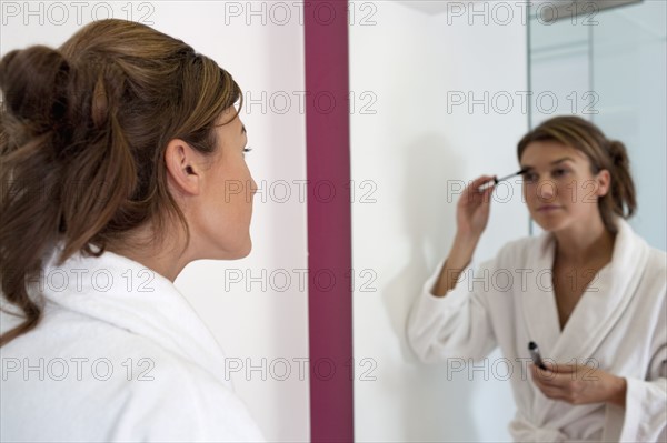 Woman applying make-up in bathroom. Photo : Jan Scherders