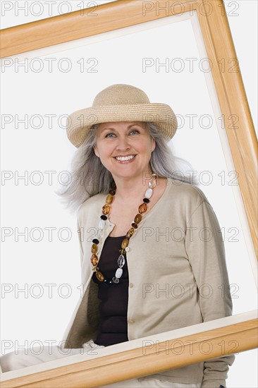 Studio portrait of mature woman behind picture frame. Photo : Rob Lewine