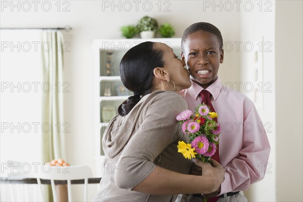 Mother kissing Son (12-13) holding bouquet. Photo : Rob Lewine