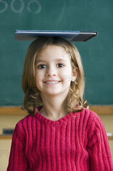 Portrait of girl (6-7) balancing book on head. Photo : Rob Lewine