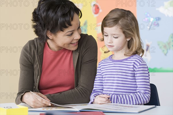 Teacher helping girl (6-7) in reading. Photo : Rob Lewine