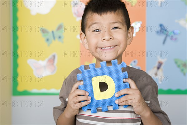Boy (6-7) holding D letter in classroom. Photo : Rob Lewine