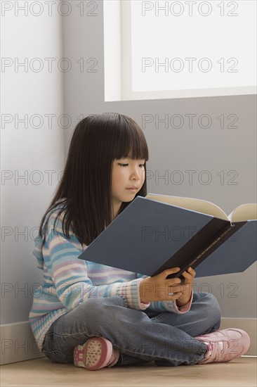 Girl (6-7) reading book in classroom. Photo : Rob Lewine