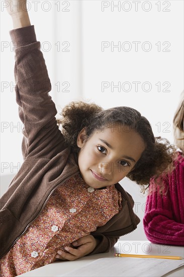 Portrait of girl (6-7) with raised hand in classroom. Photo : Rob Lewine