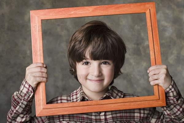 Smiling boy (6-7) looking through frame, studio shot. Photo : Rob Lewine