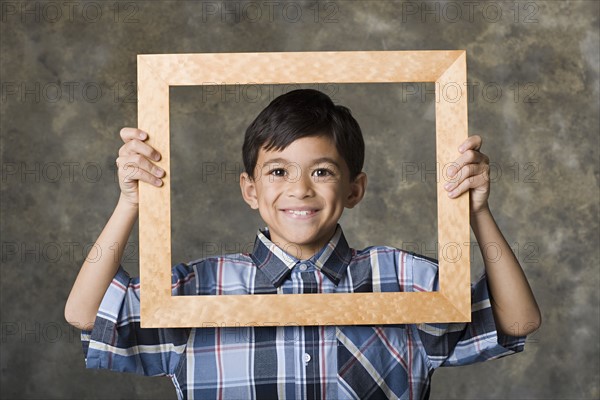 Portrait of smiling boy (8-9) looking through frame, studio shot. Photo : Rob Lewine