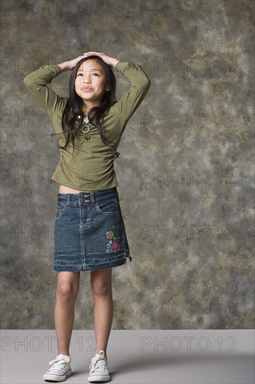 Portrait of smiling girl (8-9) with hands on head, studio shot. Photo : Rob Lewine