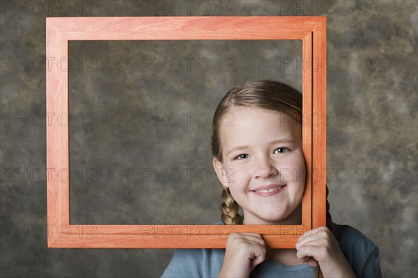 Portrait of smiling girl (8-9) holding frame, studio shot. Photo: Rob Lewine