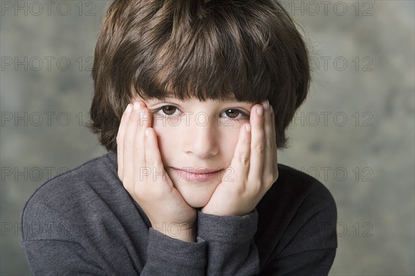 Portrait of boy (6-7) with face in hands, studio shot. Photo: Rob Lewine