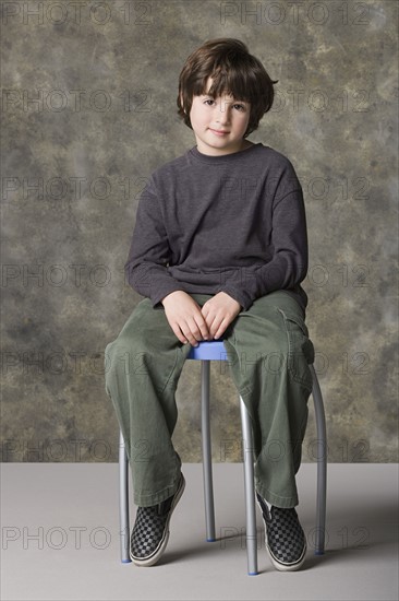 Smiling boy (6-7) sitting on chair, studio shot. Photo: Rob Lewine