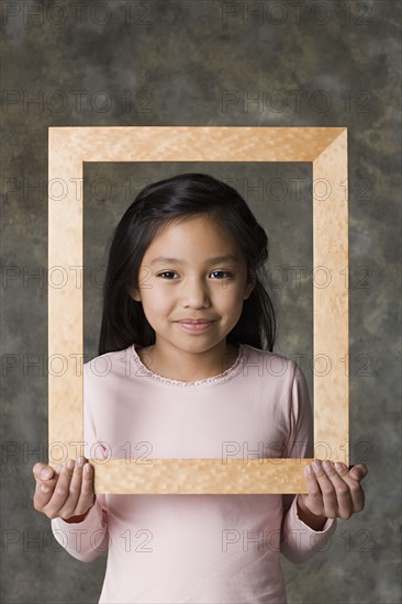 Portrait of smiling girl (8-9) holding picture frame, studio shot. Photo: Rob Lewine