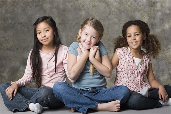 Portrait of three smiling girls (8-9) sitting together, studio shot. Photo : Rob Lewine