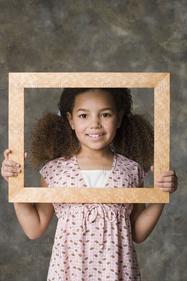 Portrait of smiling girl (8-9) holding picture frame, studio shot. Photo: Rob Lewine