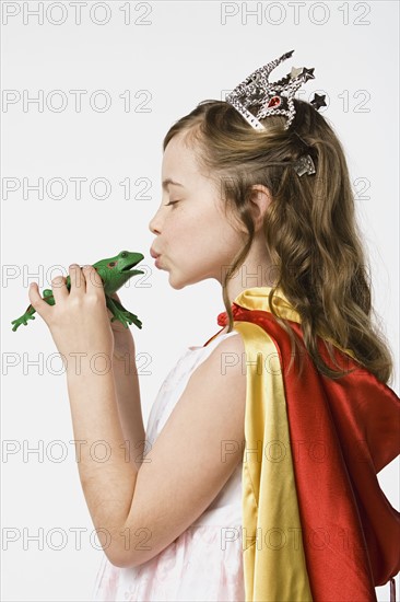 Girl (8-9) dressed as princess kissing frog, studio shot. Photo : Rob Lewine