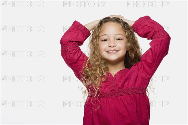 Portrait of smiling girl (8-9) with hands on head, studio shot. Photo : Rob Lewine