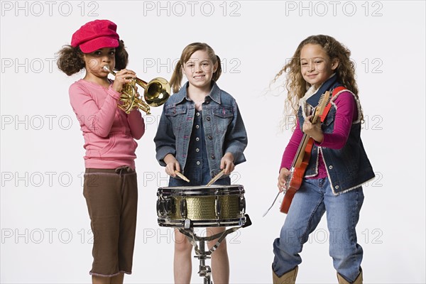 Three girls (8-9) playing instruments together, studio shot. Photo : Rob Lewine