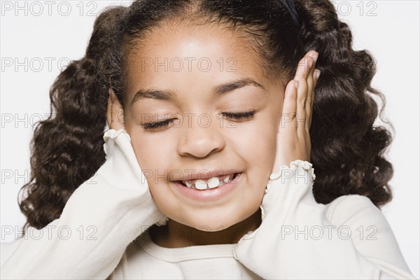 Smiling girl (8-9) covering her ears, studio shot. Photo : Rob Lewine