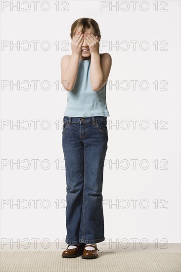 Smiling girl (8-9) covering her eyes, studio shot. Photo : Rob Lewine